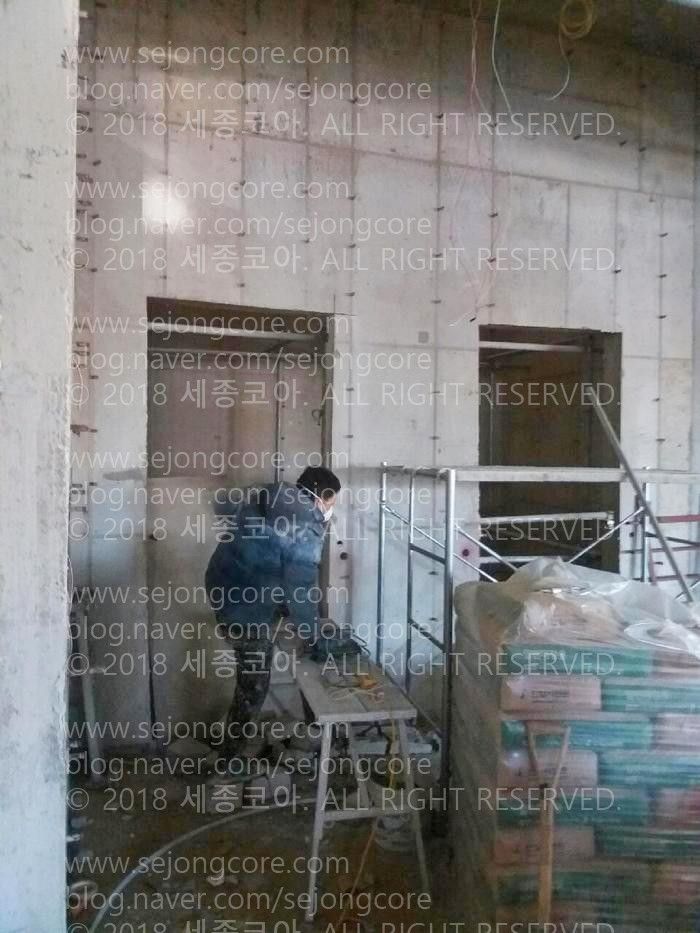 실내. 작업자가 기계를 든 상태로, 작업 발판을 밟고서 올라가고 있는 순간.